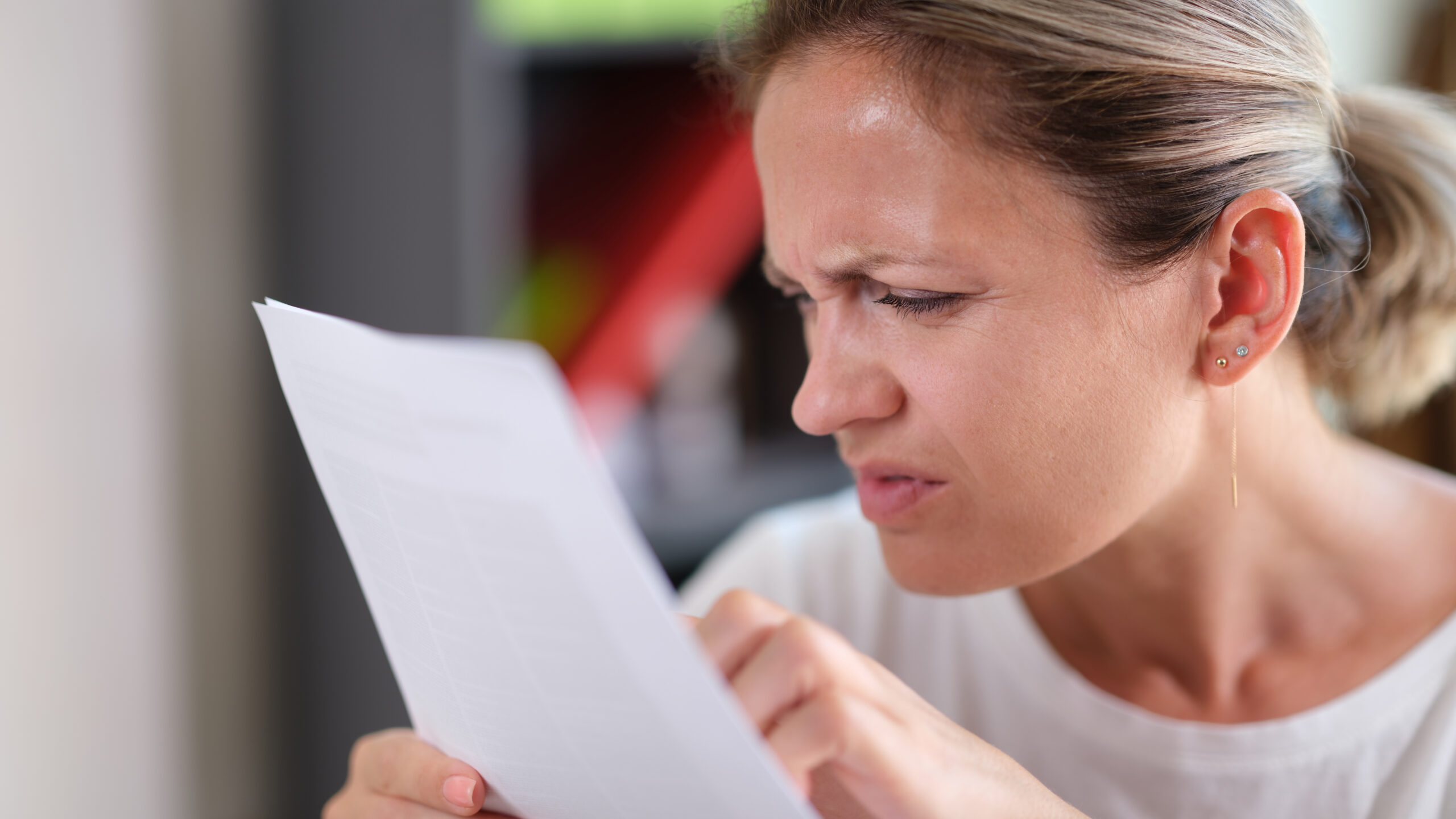 Portrait of focused female trying read text, squinting to see more clearly. Female having difficulties seeing text because of vision problems